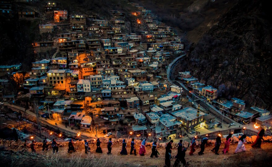 A line of men and women with torches walk along a ridge above a city nestled in the mountainside in Kurdistan.<strong> </strong>