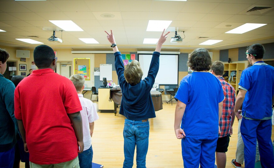 Reed (center) enthusiastically raises two peace signs while singing a tune from the Broadway musical <em>Newsies</em> during Ashley Leland's boys' chorus class at Jupiter Middle School of Technology in Jupiter, Fla.