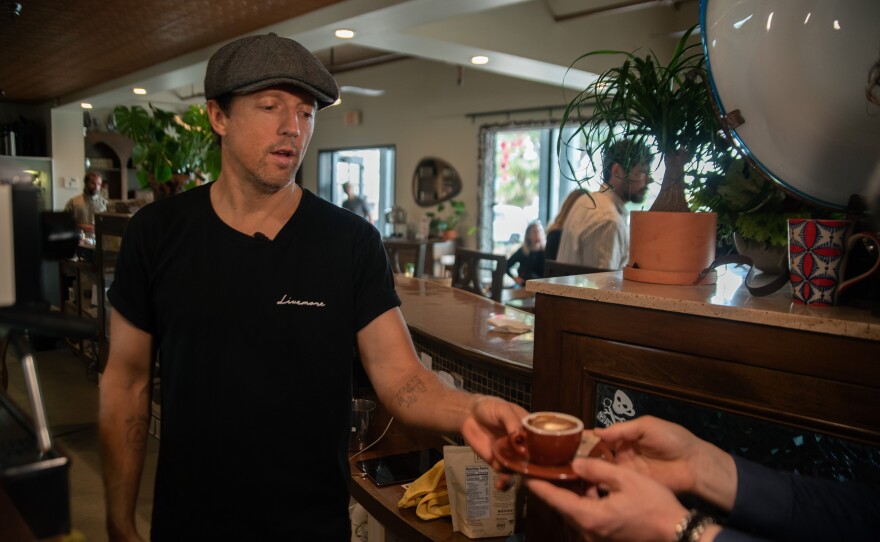 Jason Mraz hands KPBS reporter Jacob Aere an espresso at Jitters Coffee Pub in Oceanside, June 2, 2025.