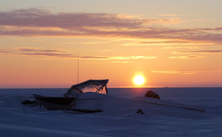 Boats buried in snow toward the edge of the lagoon at sunrise.