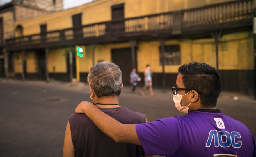 A pair of men wearing masks — but neglecting social distancing guidelines — wait for public transportation in Peru's capital, Lima. The country recently urged men and women to leave their homes only on separate days, in an attempt to slow the spread of the coronavirus.