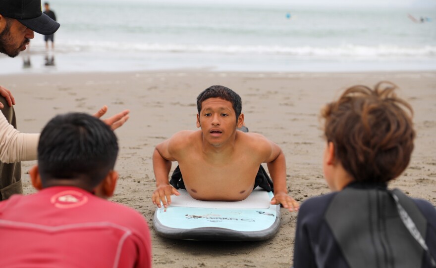 Instructor Oliver Asencio Lynes is teaching students how to stand up on a board. In the photo, he's in the starting position.