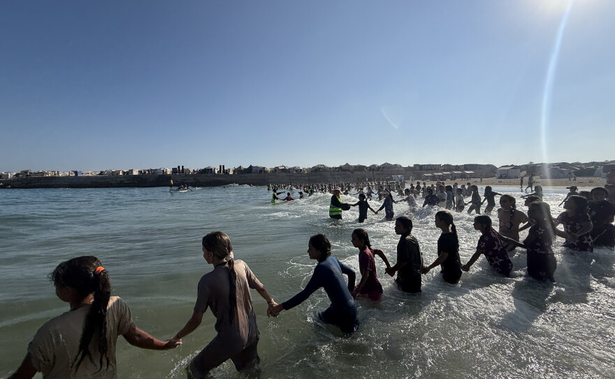 Palestinian children form a chain for a global solidarity initiative called Swim With Gaza that raises money for swimming lessons in Khan Younis on Aug. 25, 2026.