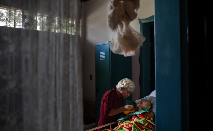 One resident helps another with lunch. The mosquito net hanging overhead will cover the bed at night, warding off bites that can spread diseases like dengue and chicungunya.