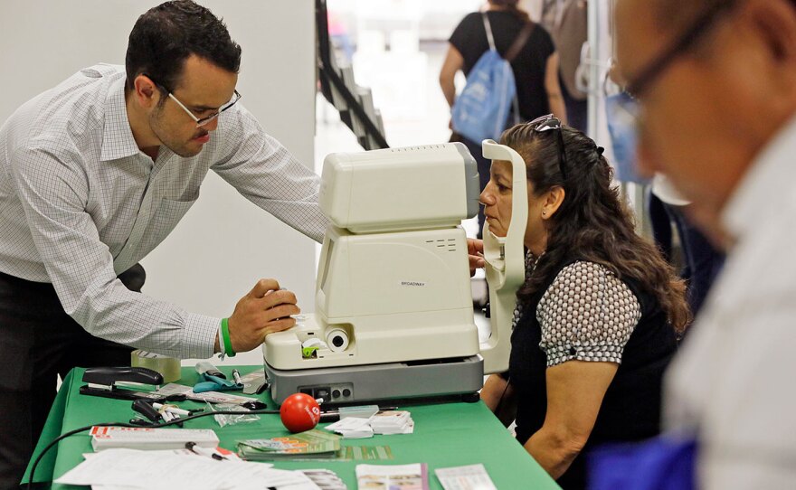 In this Oct. 1, 2013, file photo, Mexican national Rosa Guerra, right, gets a free eye exam during the Binational Health Week event held at the Mexican Consulate in Los Angeles.