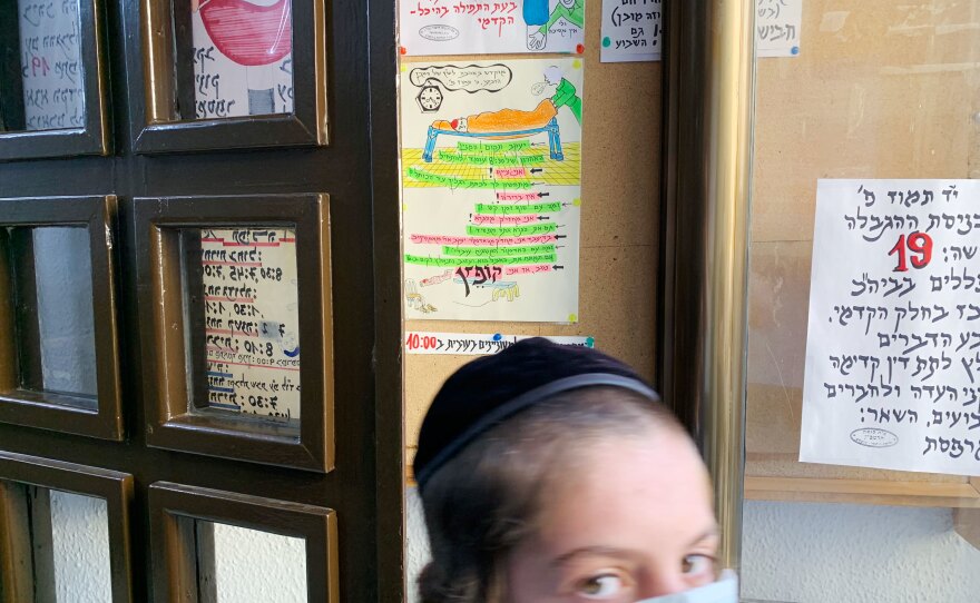 A young worshiper passes the signs and cartoons Yehezkel Cahn has tacked up at the entrance to the small synagogue. The number 19 in red (at right) indicates the maximum number of worshipers allowed indoors, per Israeli government guidelines at the time.