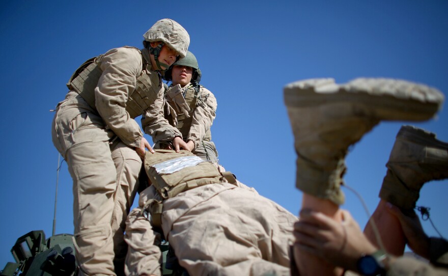 Marine Lance Cpls. Julia Carroll (left) and Paula Pineda lift "Carl" onto the LAV.