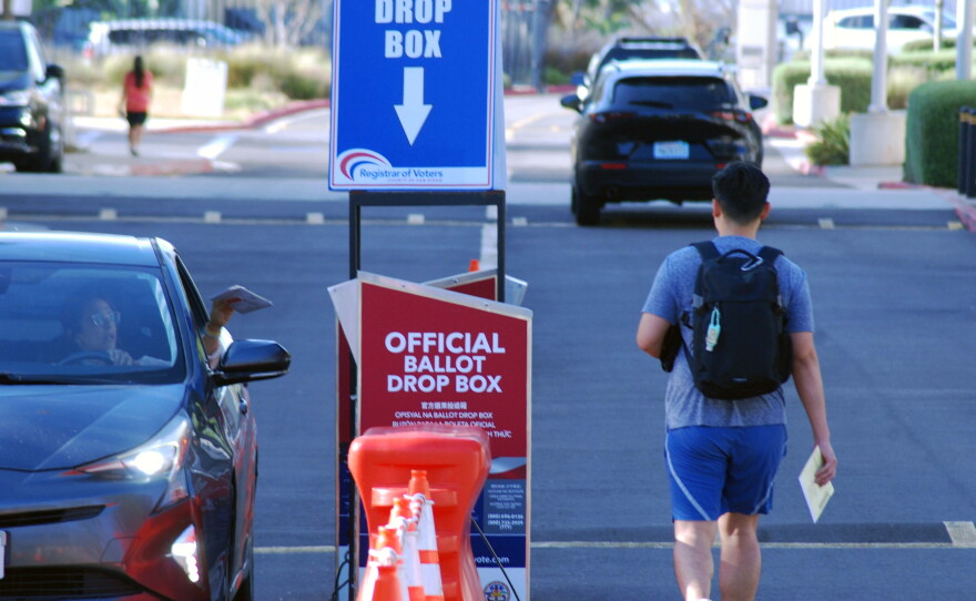 A woman drops her ballot into the drop box as a man walks up to it in Kearny Mesa on June 2, 2026.