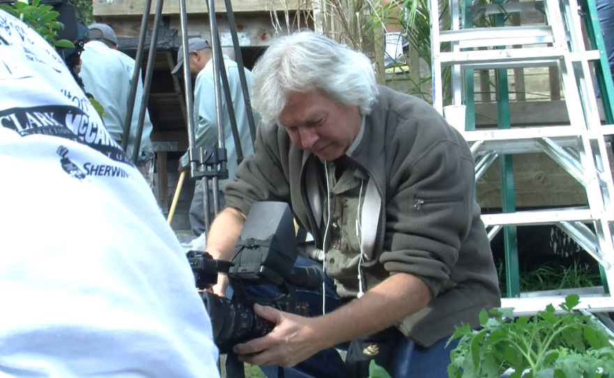 Freelance videographer Bill Bork kneels to film volunteers rehabilitating the front yard of a wounded Coast Guard veteran, April 26, 2014.