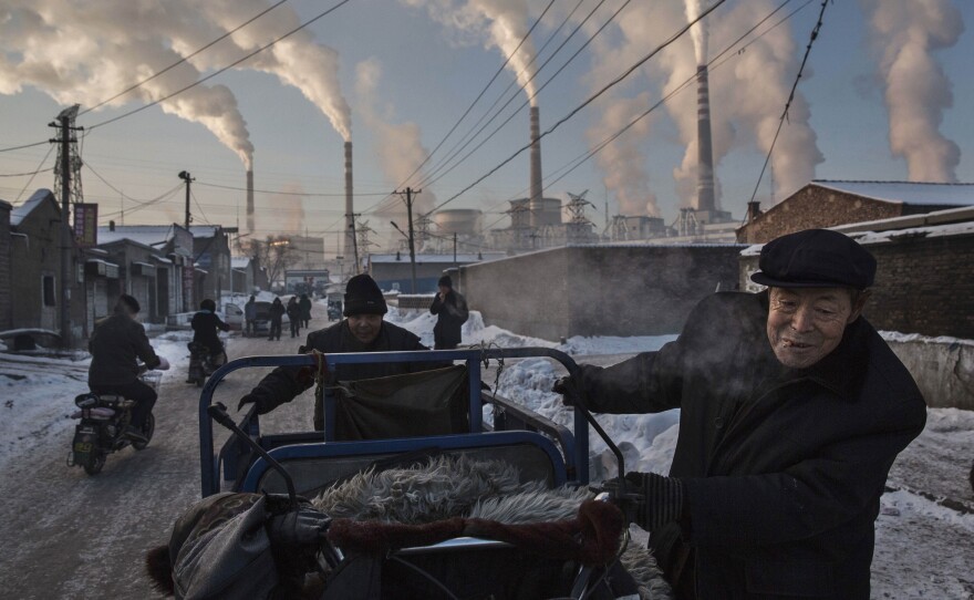 Men push a cart through a neighborhood in northern Shanxi, China, as smoke billows from a coal-fired power plant in the distance.
