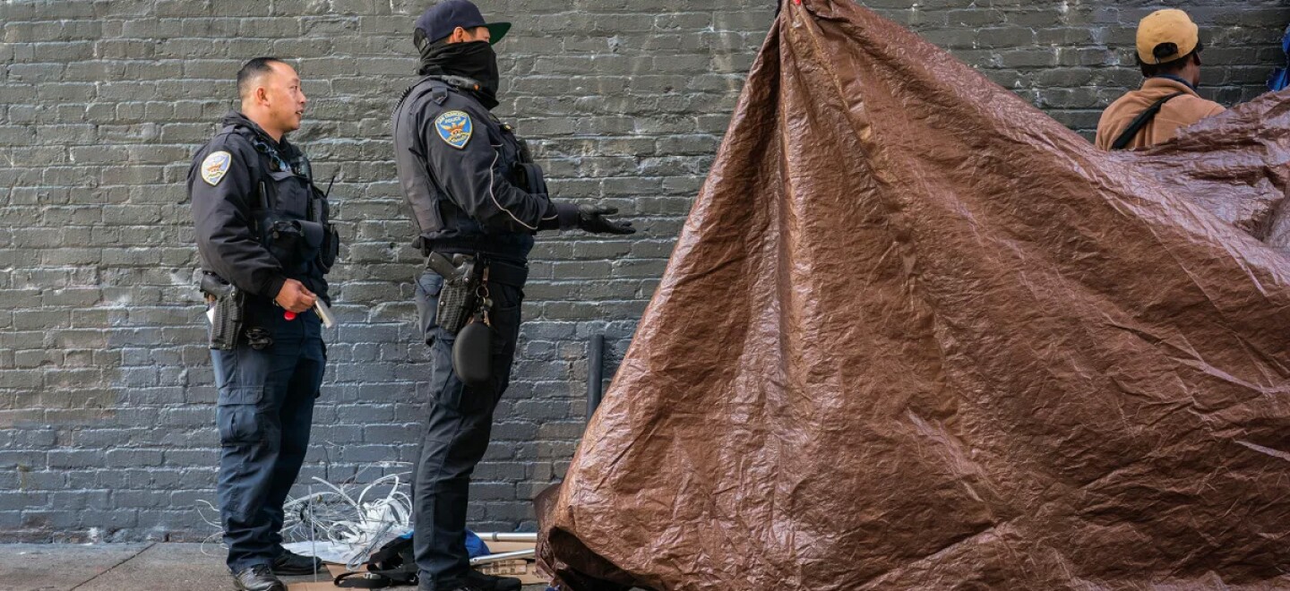 San Francisco police officers instruct an unhoused person to move personal items that are blocking the sidewalk on Cedar Street in San Francisco on Nov. 15, 2024. Unhoused people on Cedar Street are forced to move their shelters and belongings on a regular basis by San Francisco city workers.