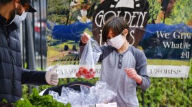 A boy wearing protective face masks to protect from the coronavirus picks out a bag of fresh produce at the North Hollywood Farmer's Market in Los Angeles on Saturday, April 4, 2020.