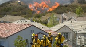 Firefighters from Glendale, Calif., and Pasadena, Calif., stand watch as bulldozers clear a firebreak near a wildfire burning along a hillside near homes in Thousand Oaks, Calif., 
