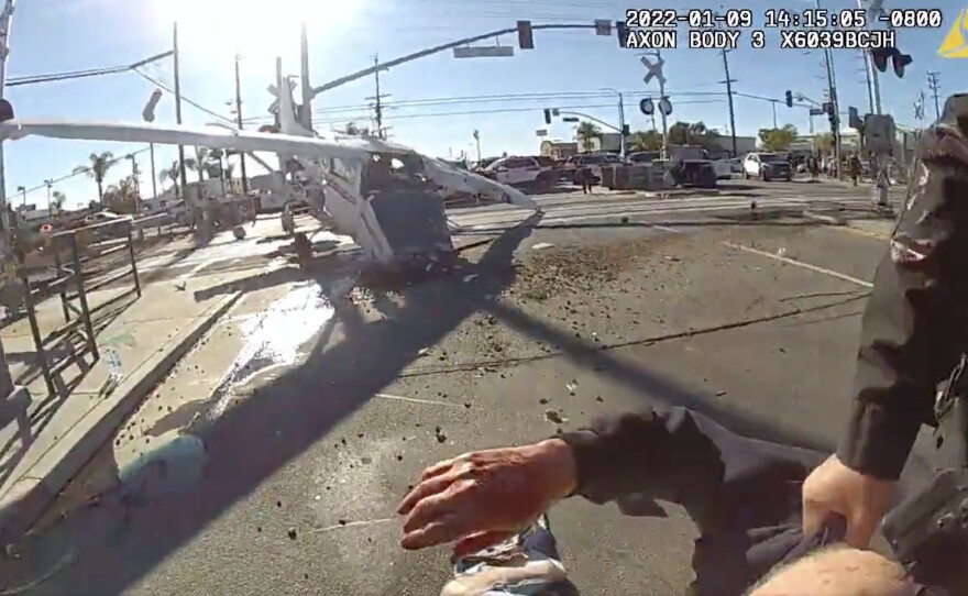 A still image from an LAPD officer's body-worn camera shows the pilot of a small plane being dragged to safety, after his aircraft crash-landed in the path of an oncoming commuter train.