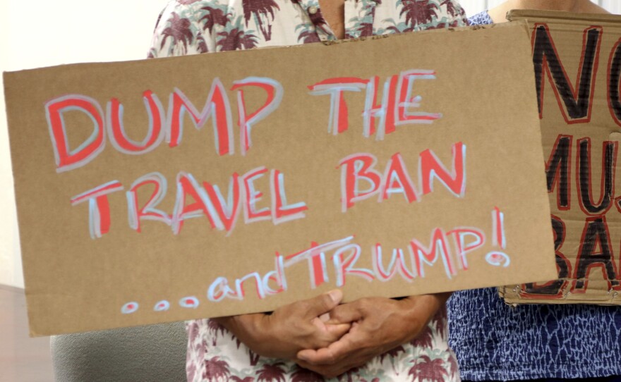 Critics of President Trump's travel ban hold signs during a news conference with Hawaii Attorney General Douglas Chin on June 30 in Honolulu.