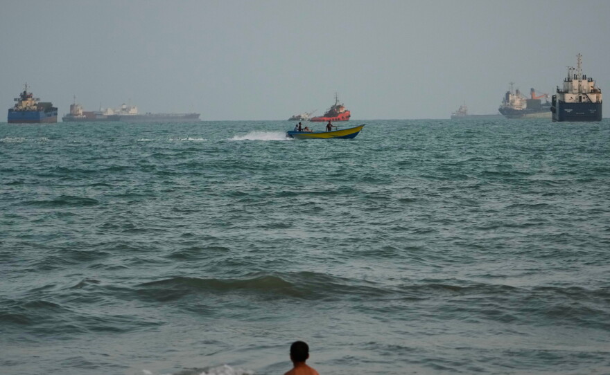A swimmer remains near the shore as a motorboat passes commercial vessels anchored in the Strait of Hormuz off Bandar Abbas, Iran, on Friday.
