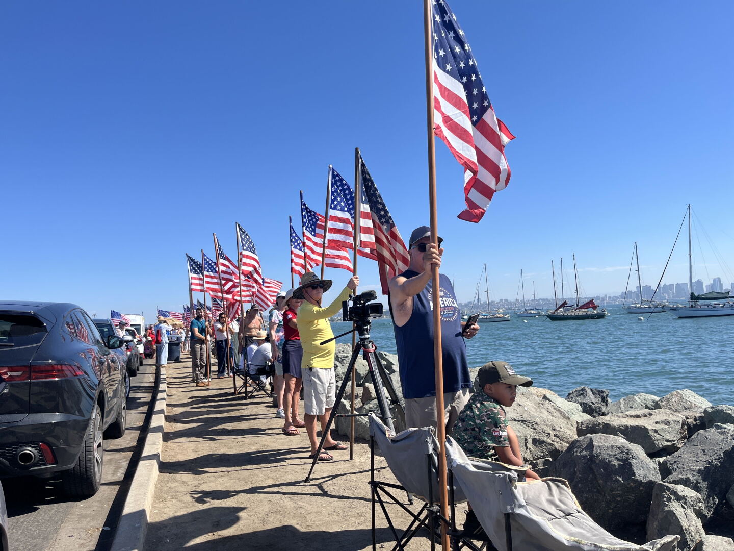 People gather with American flags along Shelter Island's shoreline ahead of the USS Lincoln's arrival on Oct. 8, 2026.