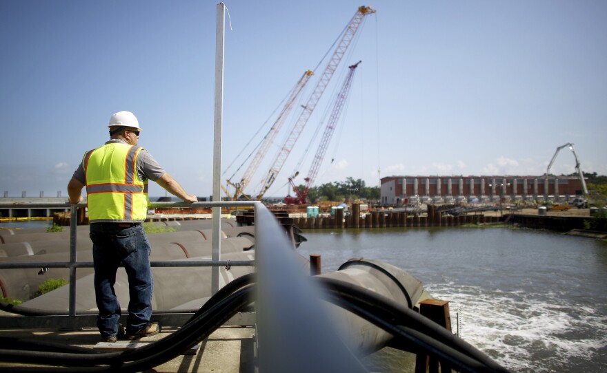 A maintenance worker watches water pour out of the temporary outflow pipes at the pumping station for the 17th Street Canal in the Orleans Levee District. The new and permanent pump house is still under construction in the distance.