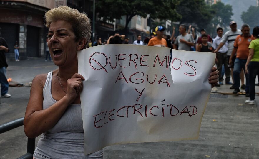 A woman holds a placard reading "We Want Water and Electricity" as she shouts slogans during a protest in Caracas, Venezuela, about a lack of water and electric service during a new power outage in the country on Sunday. President Nicolás Maduro announced a 30-day electricity rationing plan to help as the government works to restore service.