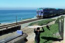 A surfer going back up the bluff in Del Mar as a Coaster train passes behind her on Jan. 21, 2022.