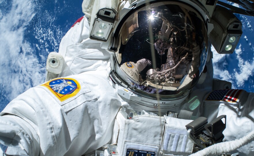 Extravehicular crewmember 2 (EV2) Terry Virts is reflected in the helmet visor of EV1 Barry Wilmore during Extravehicular Activity 29 (EVA 29). Earth is in the background.