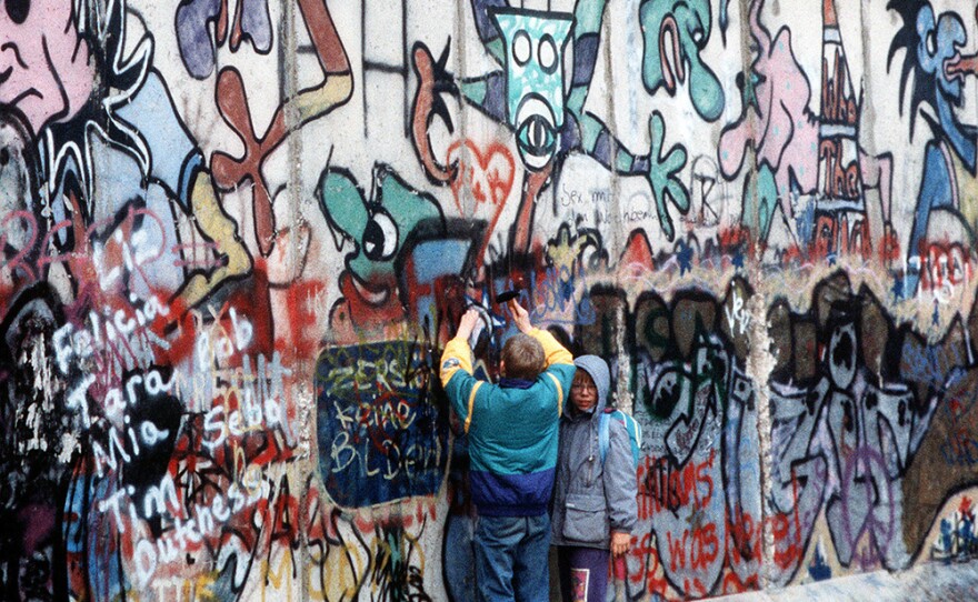West German children attempt to chip off a piece of the Berlin Wall as a souvenir.  A portion of the Wall has already been demolished at Potsdamer Platz.