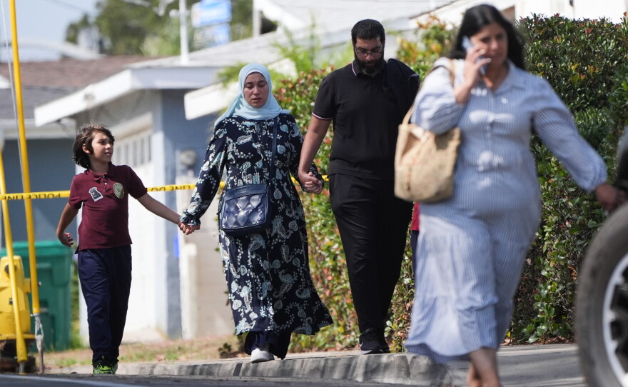 People hold hands near the scene of a shooting outside the Islamic Center of San Diego on Monday.