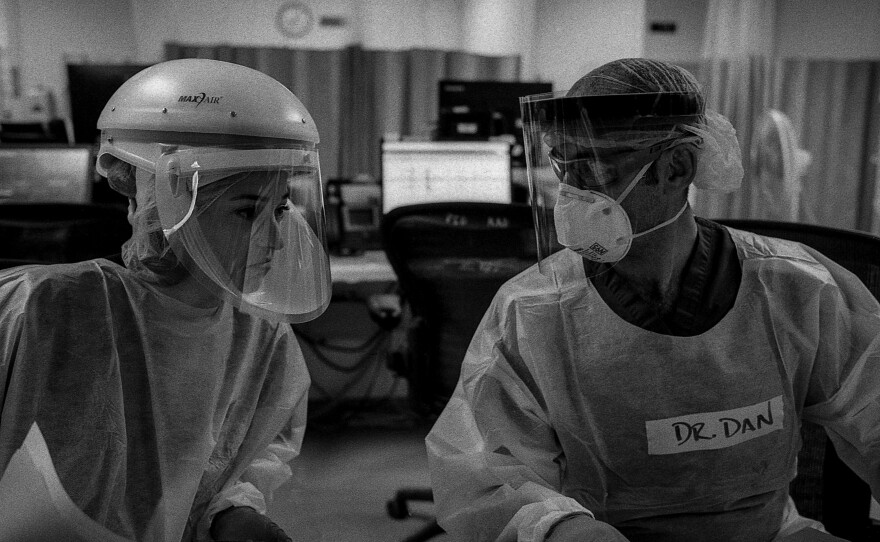 Drs. Katie Ross and Dan Dworkis discuss the care of several patients in the emergency department's COVID-19 unit. The doctors' muffled voices are hard to hear over the sound of air filtration units humming and monitors alarming.
