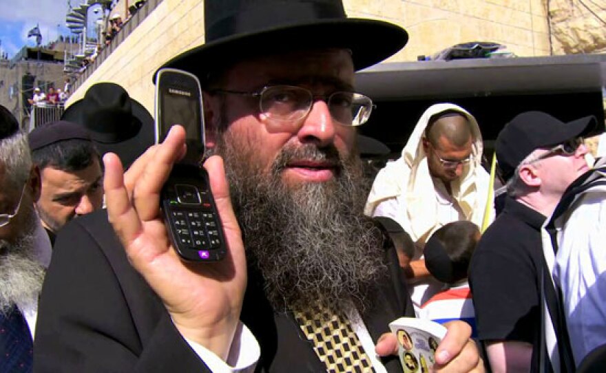 Modern technology (man holding a mobile phone) meets ancient traditions at the Western Wall in Jerusalem.