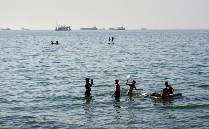Residents swim and play in the waters of the Strait of Hormuz while cargo ships and commercial vessels lie anchored in the distance off Bandar Abbas, Iran, Wednesday, June 10, 2026.