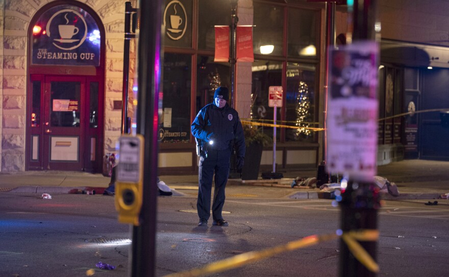 A police officer uses a flashlight while looking for evidence in downtown Waukesha, Wis., after an SUV sped through a barricade and slammed into a Christmas parade, injuring multiple people Sunday, Nov. 21, 2021.