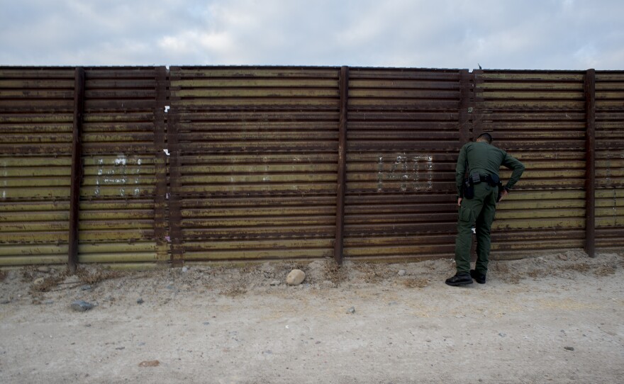Eduardo Olmos, a Border Patrol public affairs officer, peers through a section of primary fencing between the San Ysidro and Otay Mesa ports of entry in San Diego on Aug. 16, 2017.