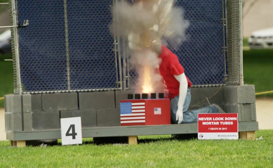 A still frame from a Consumer Product Safety Commission video shows a mannequin's head leaning over an active fireworks display.