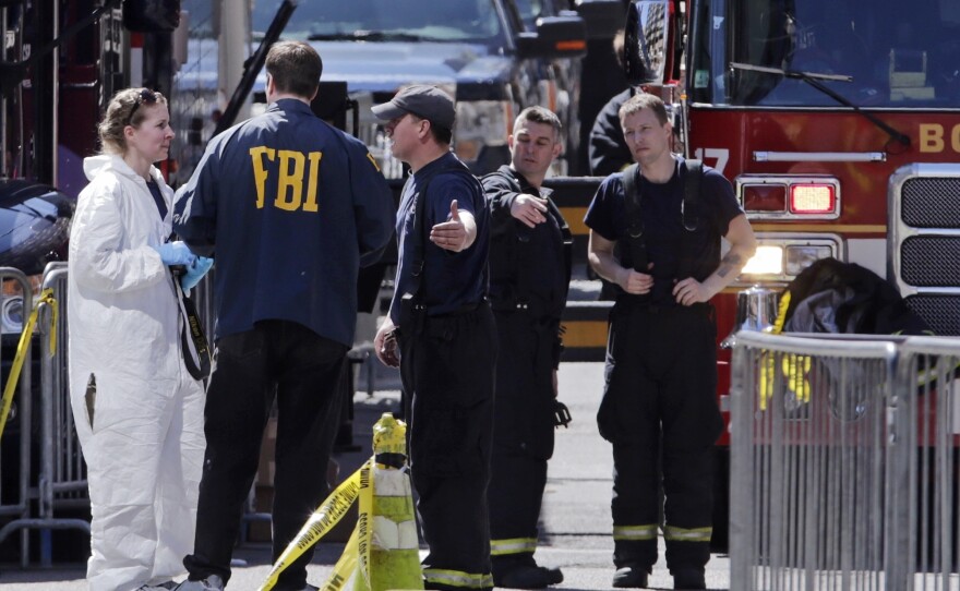 Boston firefighters, right, talk with FBI agents and a crime scene photographer on Tuesday at the scene of the Boston Marathon explosions.
