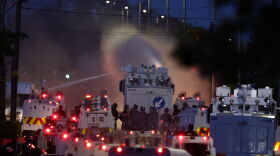Police fire a water cannon towards rioters after they set fire to wheelie bins and removed a garden fence to use as a shield against the water cannon in Newtownabbey, Belfast, Northern Ireland, Wednesday June 10, 2026.