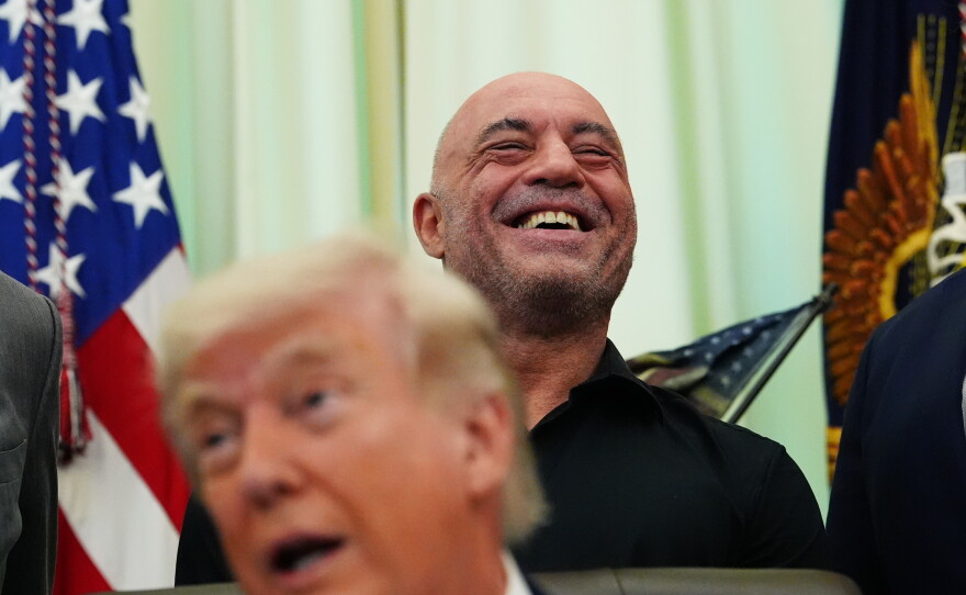 Joe Rogan laughs as President Donald Trump speaks in the Oval Office of the White House on April 18, 2026.
