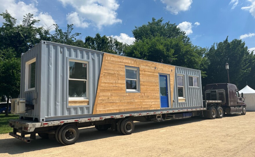 A tiny house made from a shipping container arrives on the Mall, transported by truck.