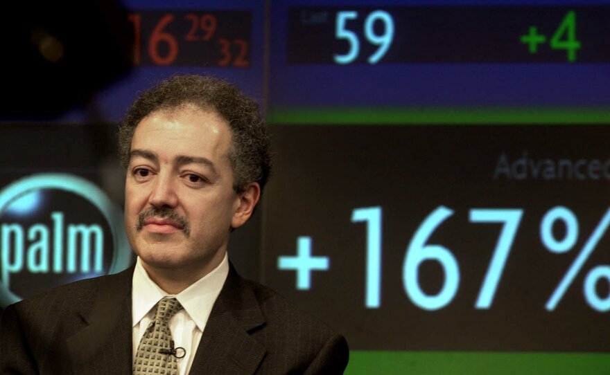 3Com's Chief Executive Eric Benhamou, listens during an interview at Nasdaq television studios in New York, March 2, 2000. A stock ticker shows shares of Palm Inc., a spinoff of 3Com, soaring in opening trading on the Nasdaq Stock Market.