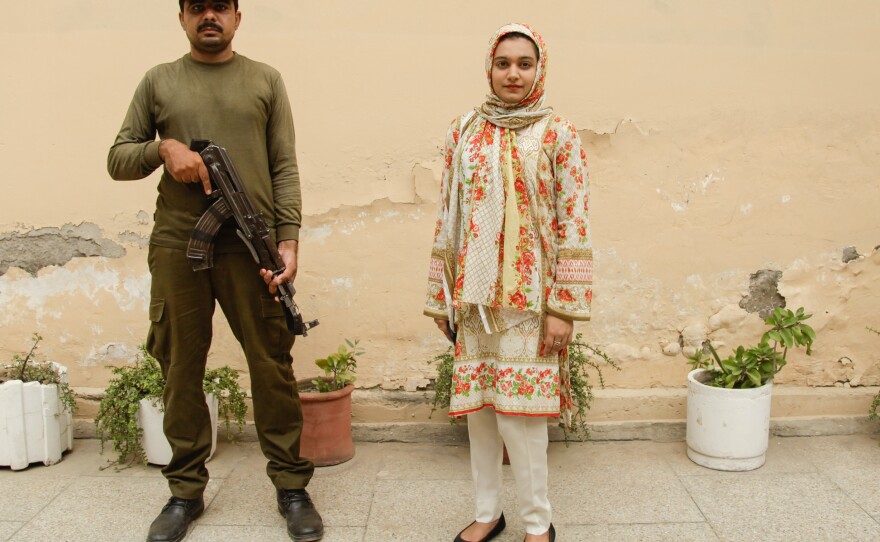 Khadija Saddiqi, 22, stands outside her family home with an armed guard who was assigned to protect her by the wife of the chief minister of Punjab. Saddiqi won a case against a classmate who tried to stab her to death in May last year after she ignored his advances.