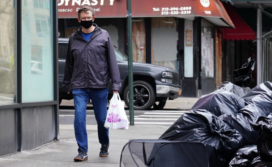A man wearing a protective mask looks at piled-up trash in New York City on April 24. Cities are struggling with collection as the volume of residential garbage surges during the stay-at-home era.