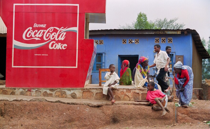 A group of Rwandans waits for transportation near a Coca Cola placard. The photo is from 1994.