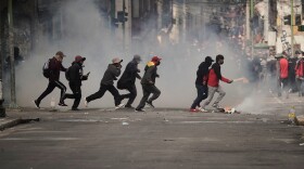 Demonstrators run across a street during an anti-government protest in La Paz, Bolivia, Monday, May 18, 2026.