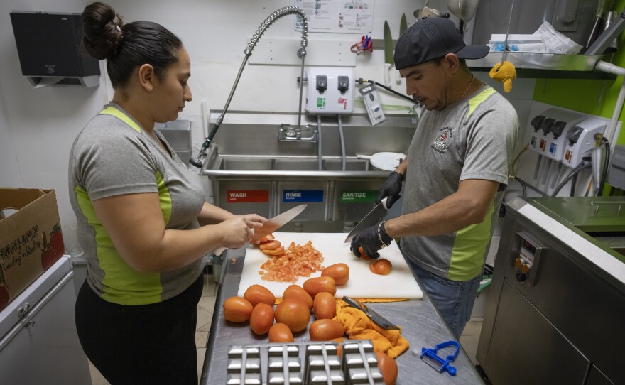 Vazquez, right, and an employee cut tomatoes in the kitchen of his shop.