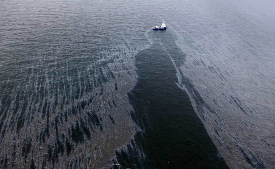 A boat with an oil boom tries to contain the spill, approximately seven miles from where the oil rig sunk last week.