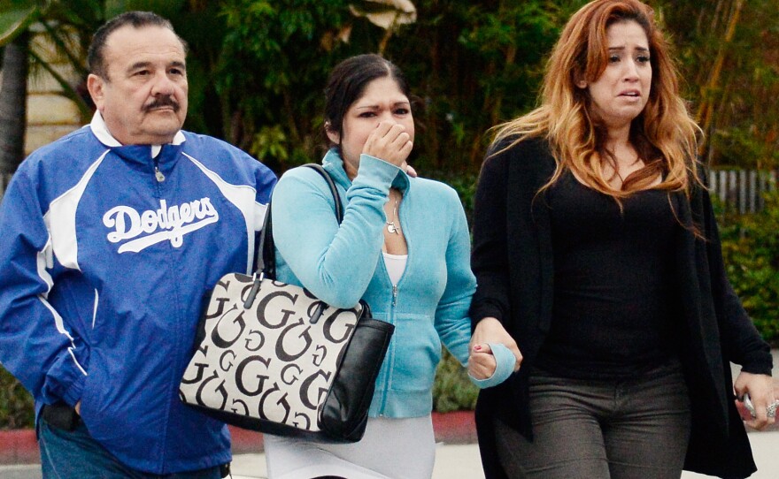 Relatives of two victims near the scene of an SUV that crashed after the driver was shot. The driver was killed and a passenger seriously injured.