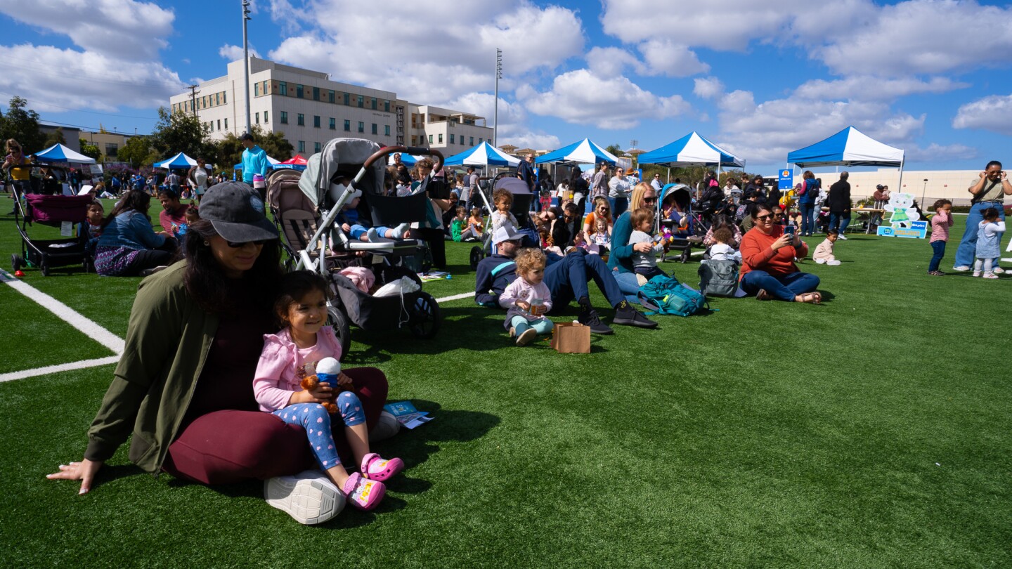 Families sit to enjoy live performances on the field at Be My Neighbor Day across the street from the KPBS station on Saturday, April 6 in San Diego, CA.