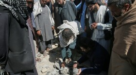 Residents and Taliban police gather the remains of a projectile at the site of a strike in Kabul, Afghanistan, on March 13.