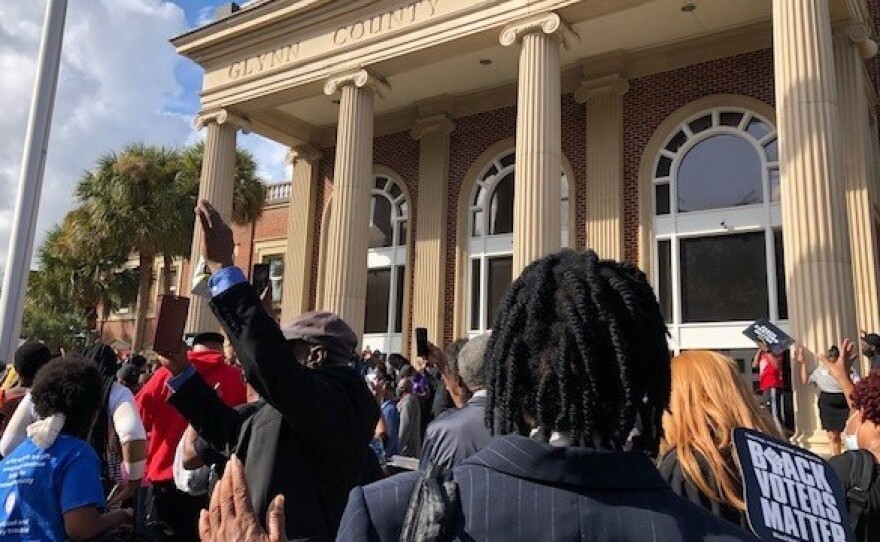 Attendees raise their hands in prayer during a rally outside the Glynn County Courthouse, where the three men accused of murdering Ahmaud Arbery are on trial.