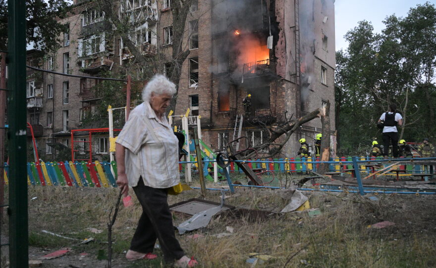 A woman walks past a burning apartment building after a Russian missile attack in Kyiv, Ukraine, Thursday, July 2, 2026.
