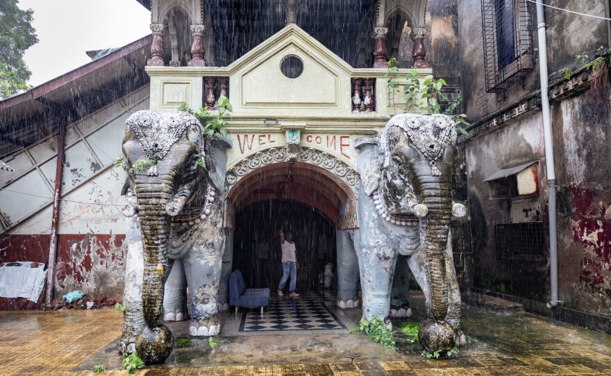 Elephant statues and a security guard stand at one of the entrances of the Imperial Cinema, locked behind heavy metal gates.